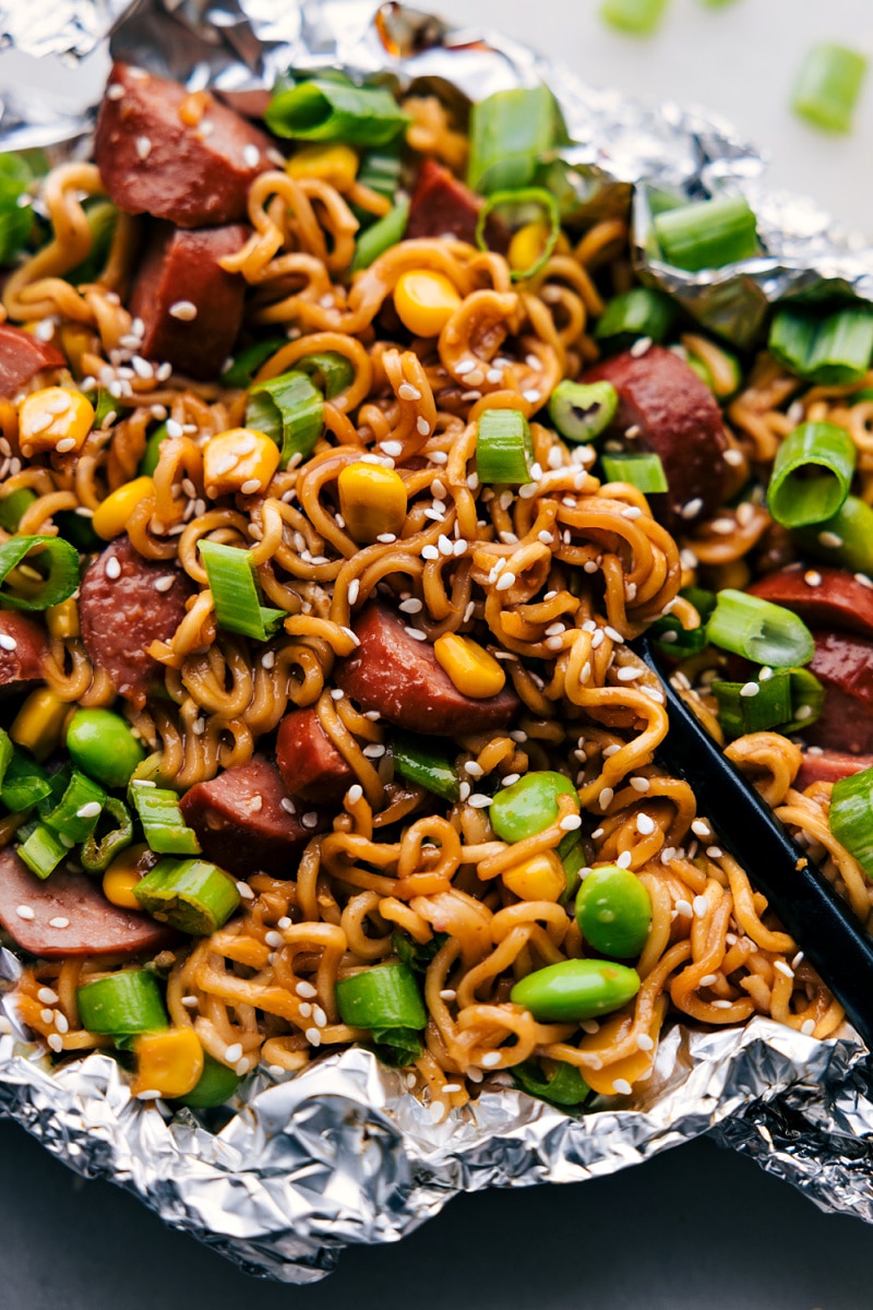 Delicious Foil Pack Ramen Noodles recipe is an explosion of flavors, all conveniently packed into a single foil package. The dish unites the umami-rich, spicy, and slightly sweet notes of a quick homemade stir-fry sauce with the smokiness of sausage, freshness of veggies, and the comforting familiarity of ramen noodles.ย Recipe via chelseasmessyapron #dinner #quick #easy #simple #familyfriendly #kidfriendly #easycleanup #camping #campingfood #foilpack #ramennoodles Up-close overhead image of the Ramen Noodle Foil Packs