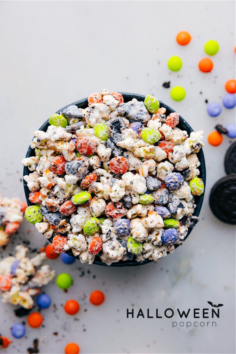 Halloween Popcorn is the go-to treat for Halloween, packed with fun and flavor! Imagine freshly popped popcorn coated in creamy white chocolate, dotted with crunchy M&M's, and decked out with festive Oreos. Beyond being insanely delicious, it also stands out as a great party centerpiece! Recipe via ChelseasMessyApron.com #halloween #popcorn #treats #M&Ms #Oreos #kidfavorite #whitechocolate Overhead view of a bowl of Halloween Popcorn