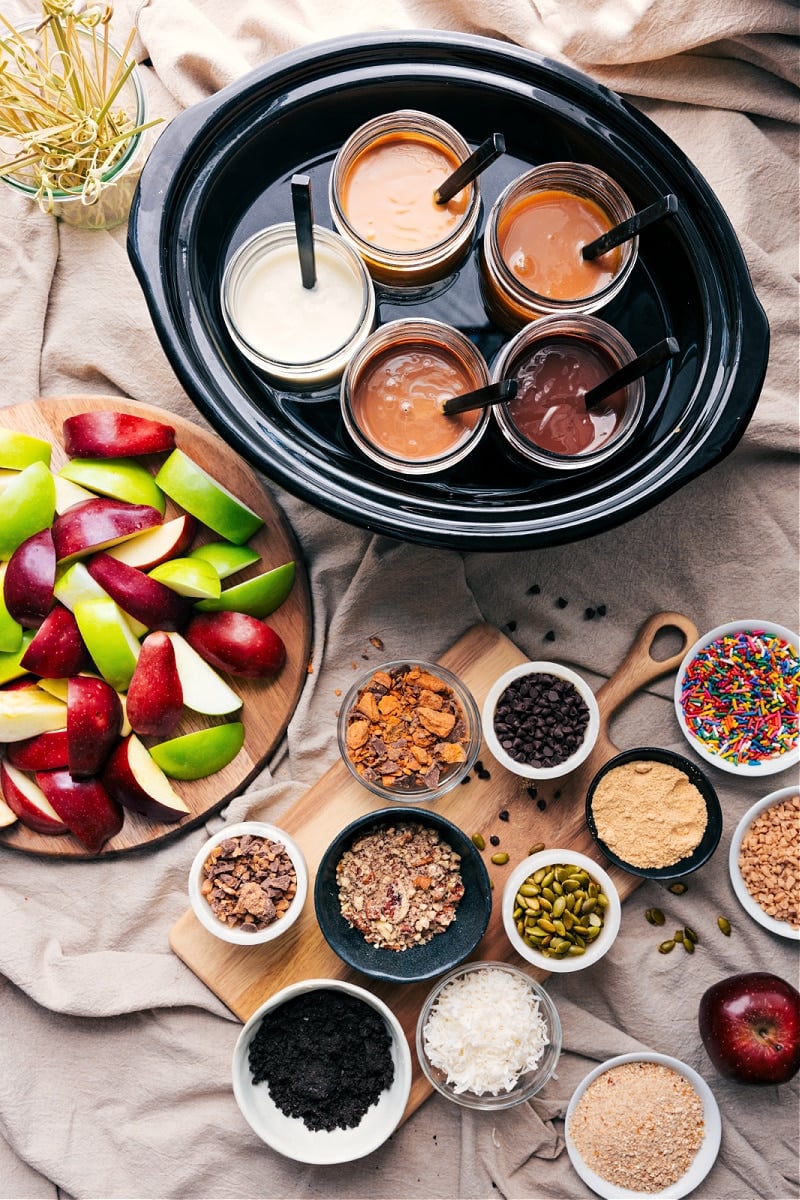 Get into the Fall spirit with our easy-peasy Caramel Apple Bar guide. We've got the best dips, favorite toppings, and a sneaky trick to keep those apples looking fresh and crisp all evening long! Whether it's a relaxed autumn night, a party, shower, or just 'cause you feel like it, this dessert station is a hit every single time! Recipe via chelseasmessyapron #dessert #best #quick #easy #simple #treat #familyfriendly #babyshower #weddingshower #fall #fallrecipes #falltreats #caramel #apple #bar #caramelapplebar Overhead image of the caramel apple bar