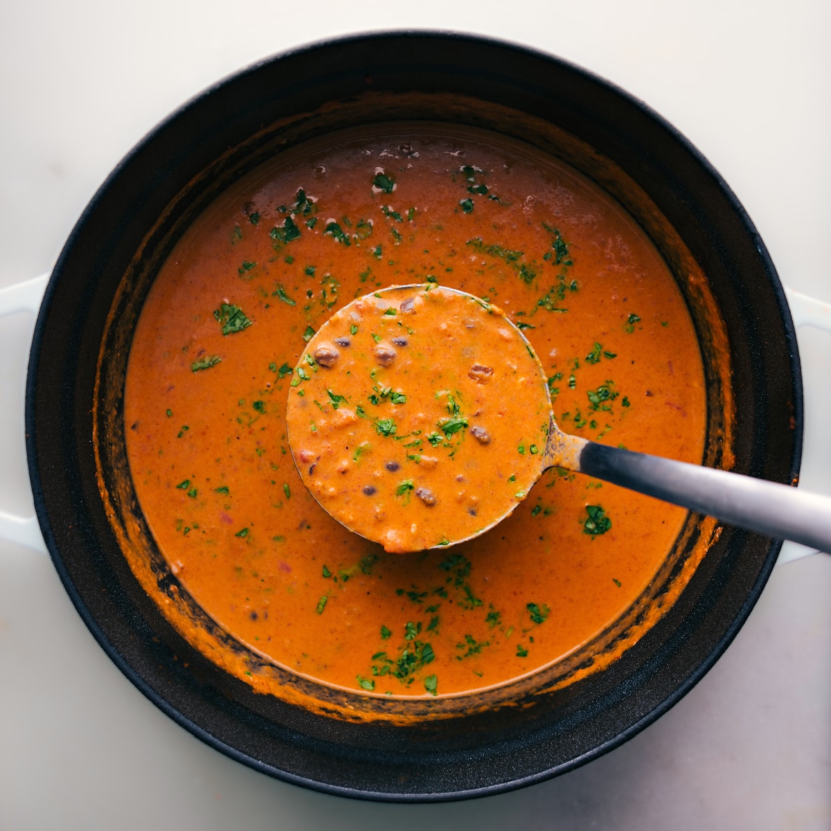 Serving Pumpkin Black Bean Soup from the Pot Overhead view of Pumpkin Black Bean Soup in a pot with a ladle scooping a serving.