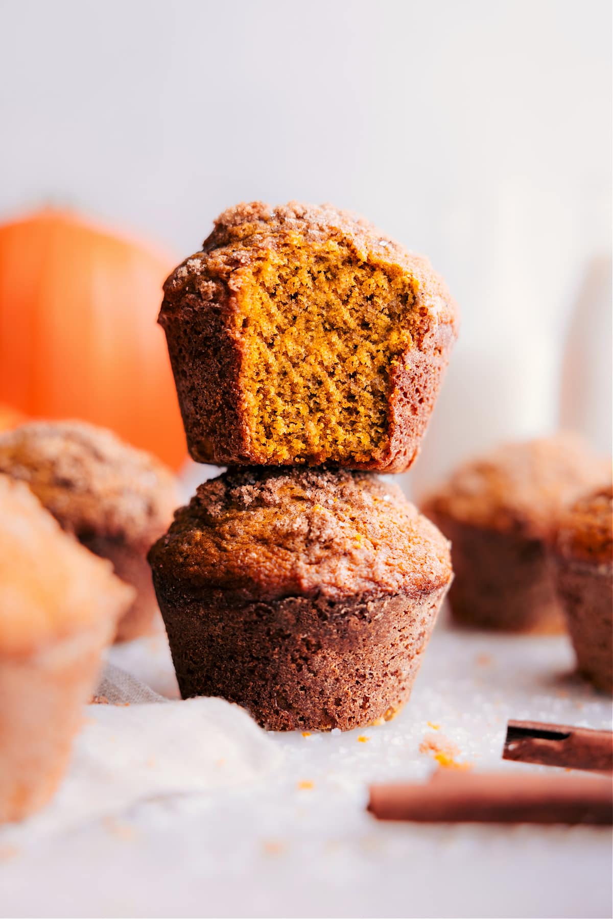 Stacked Pumpkin Muffins, One Partially Eaten A stack of pumpkin muffins with a warm, golden tone, one at the front displaying a bite taken, revealing the moist interior.