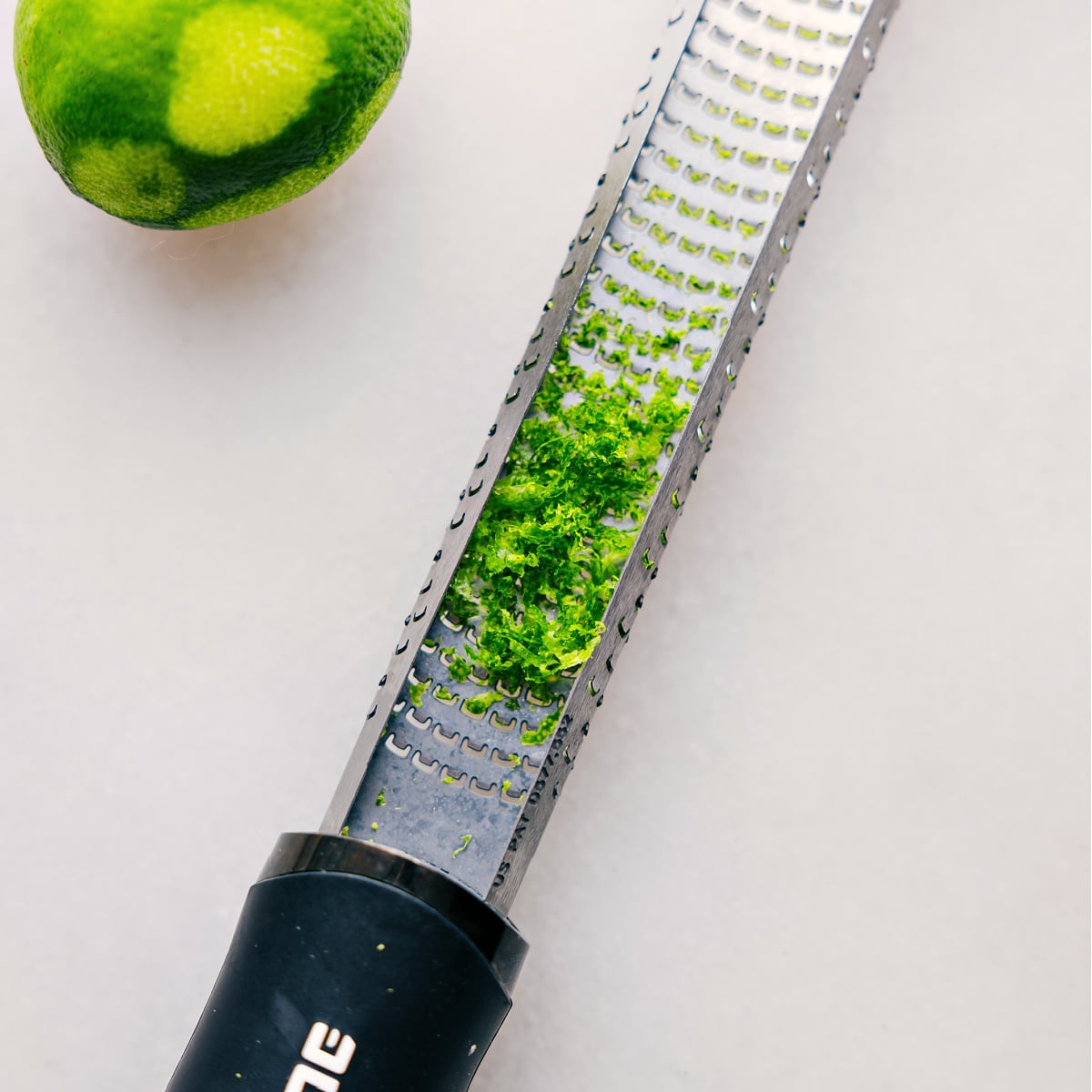 Fresh Lime Zest: Unlocking Vibrant Citrus Flavors with a Zester! A zester tool covered in fine lime peel shavings, highlighting the fresh, green zest just removed from the fruit, ready for use in this recipe.