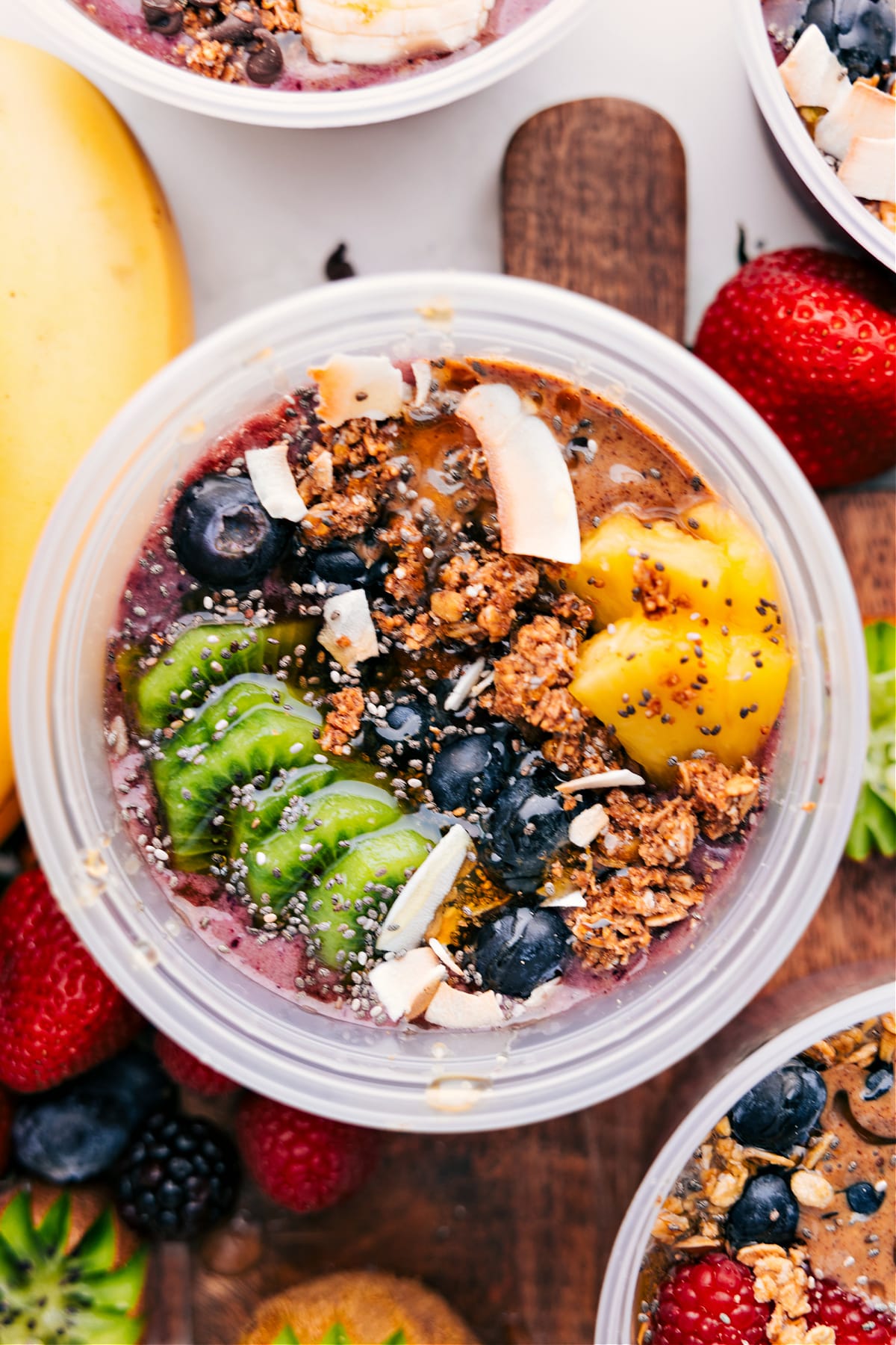 Tropical Acai Bowl Recipe Tropical acai bowls recipe with kiwi, blueberries, pineapple, coconut flakes, granola, chia seeds, and honey.