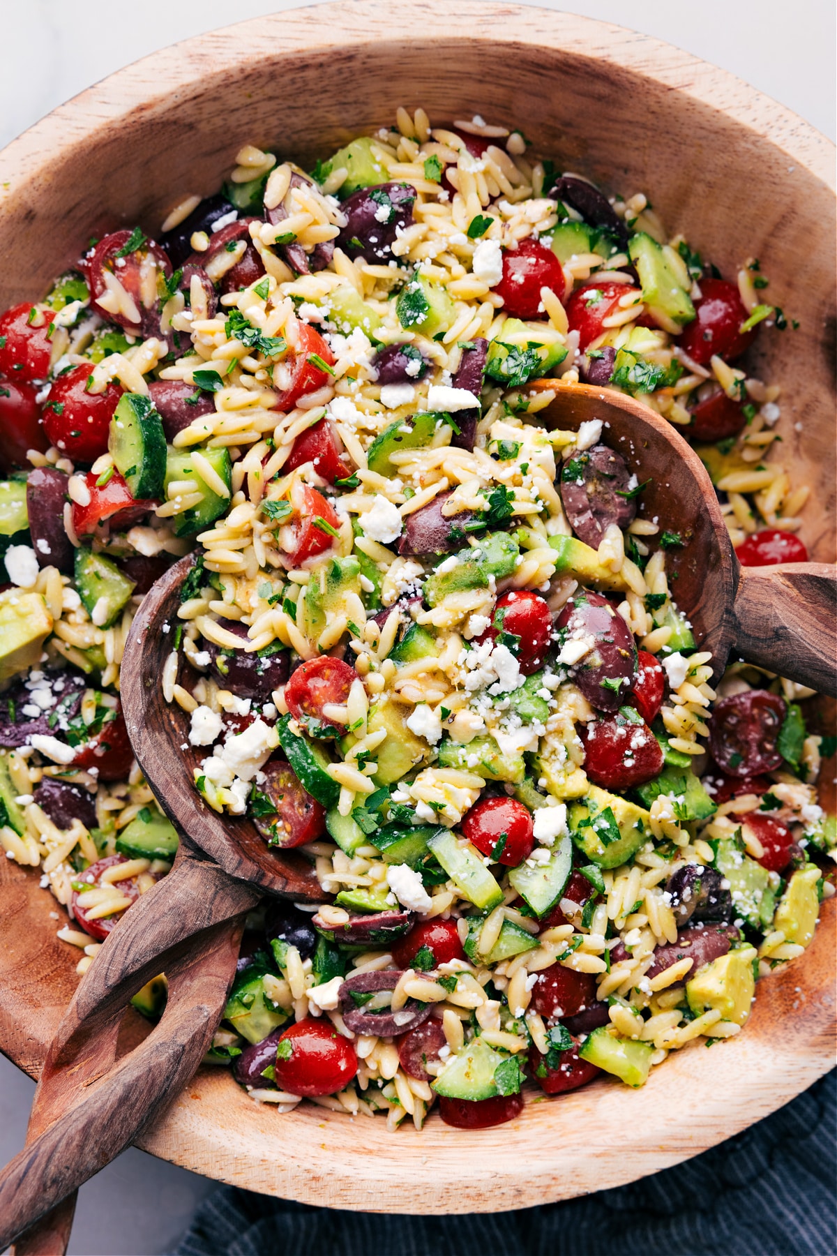 Mediterranean Orzo Salad Wooden spoons, tossing a batch of Mediterranean Orzo Salad.