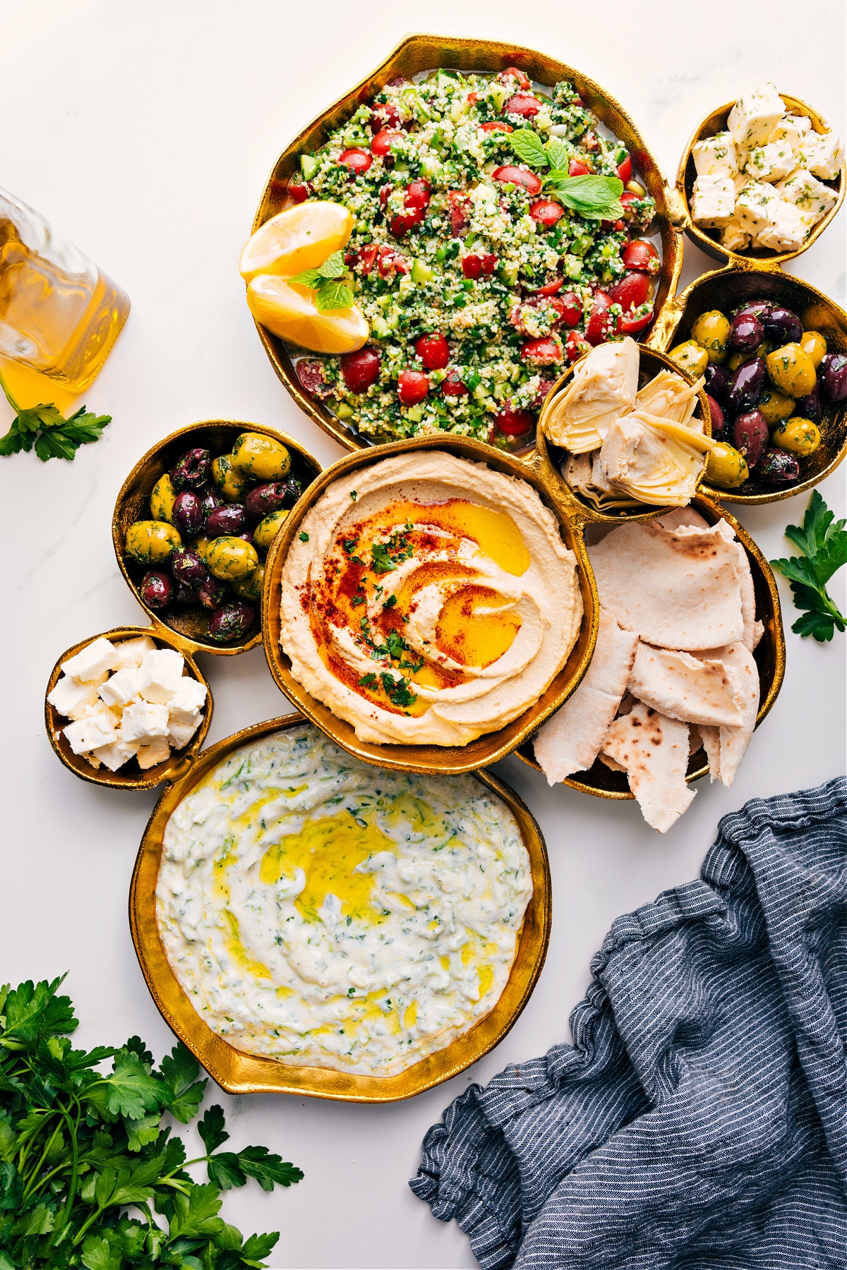 A gold serving platter filled with dips, salad, and cheeses.