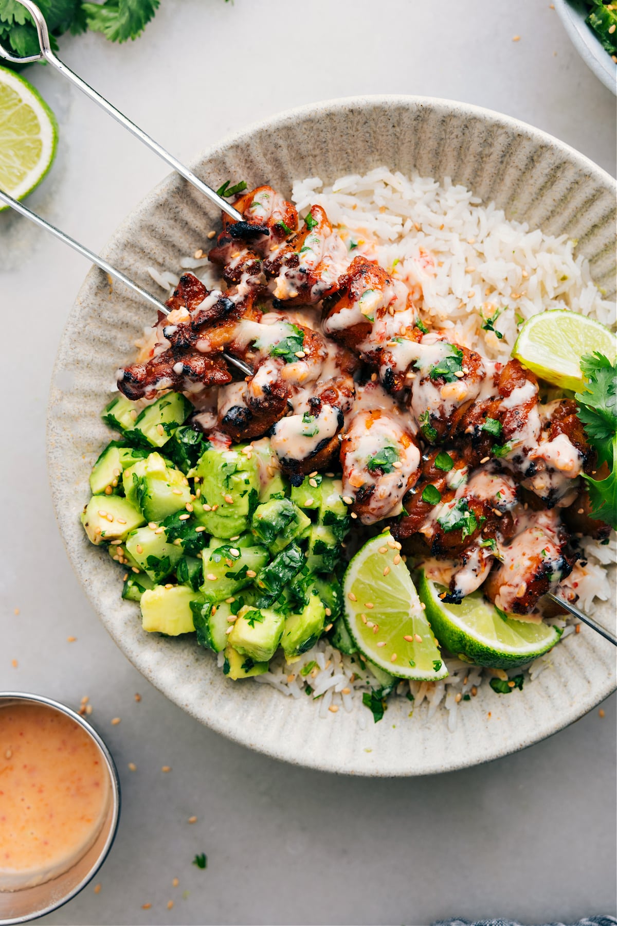 The Best Bang Bang Chicken Skewers Recipe Bang Bang Chicken Skewers sit on a bed of rice, topped with bang bang sauce, and paired with a cucumber avocado salad on the side.