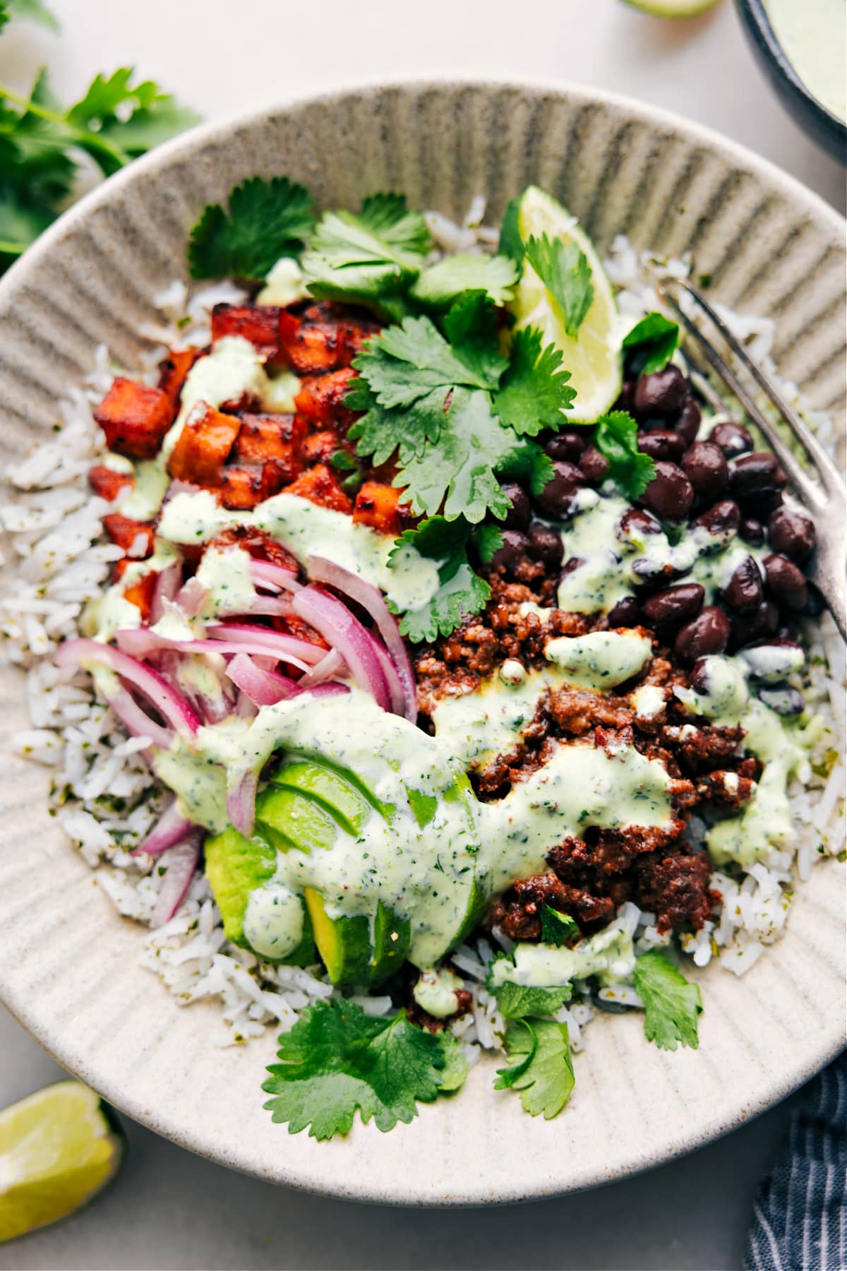The Perfect Meal Prep: Beef Burrito Bowl Recipe Beef burrito bowl recipe with cilantro lime sauce drizzled over it.