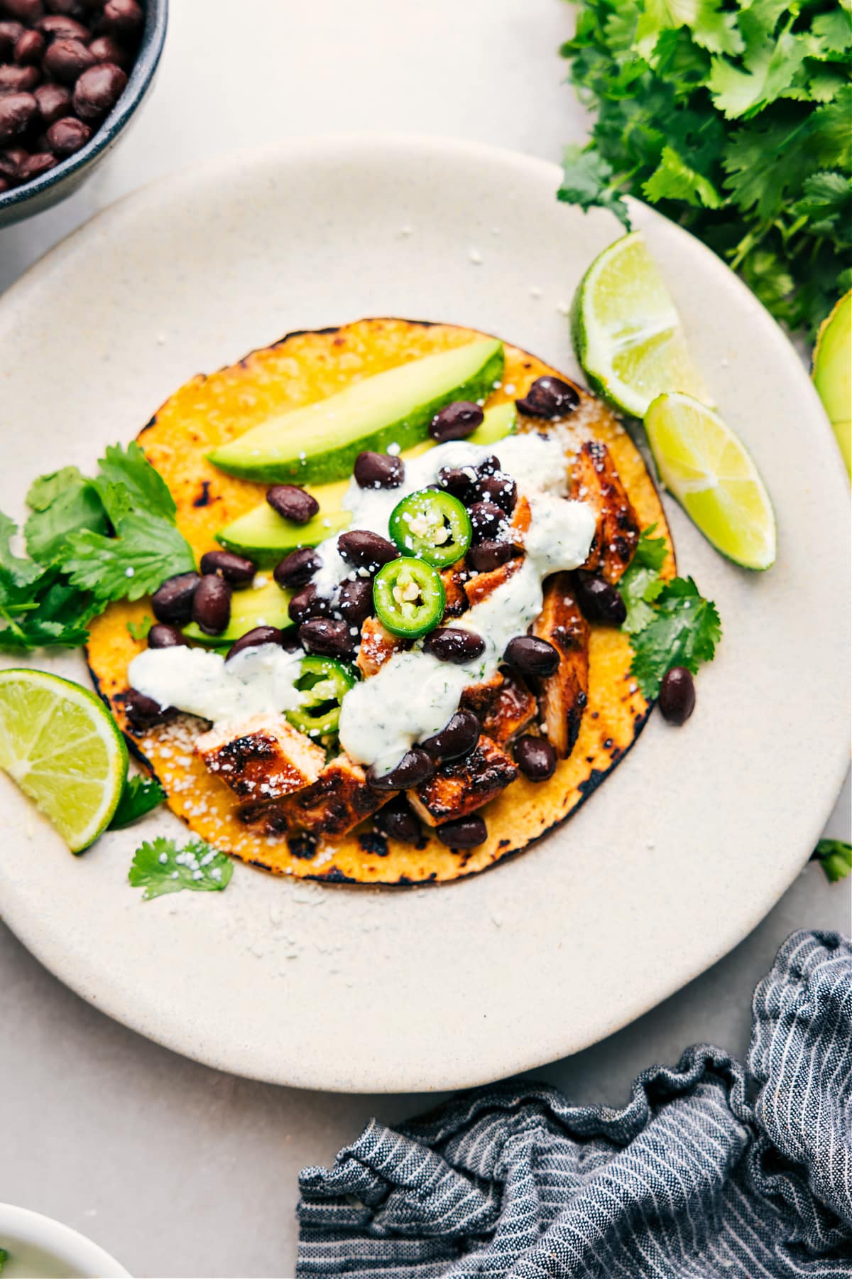 Chicken Taco Marinade wrapped in a tortilla and topped with sauce, beans, avocado, fresh jalapeño, and cilantro.
