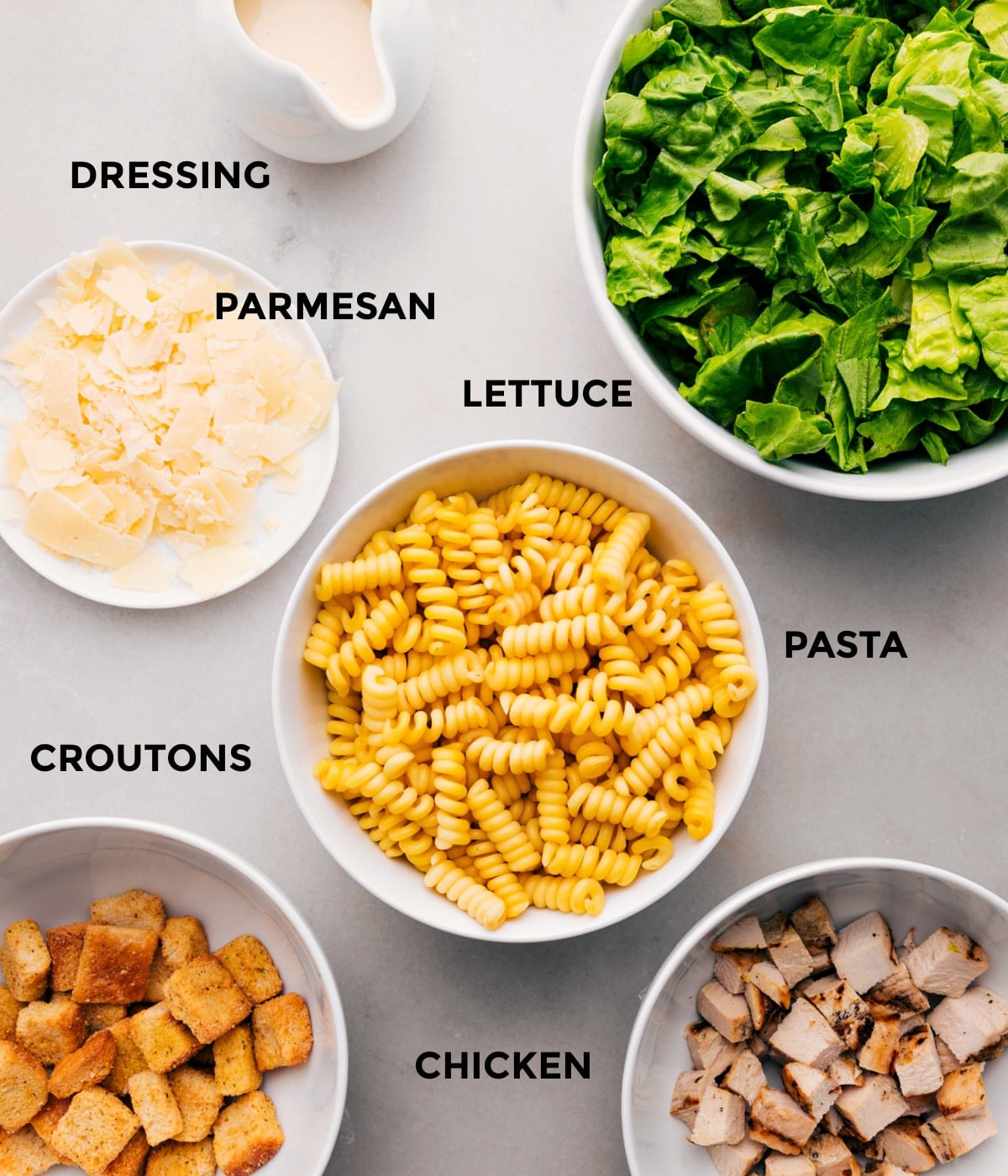Ingredients In Chicken Caesar Pasta Salad All the ingredients for this recipe prepped and ready for easy assembly, including the dressing, parmesan, lettuce, pasta, chicken, and croutons.