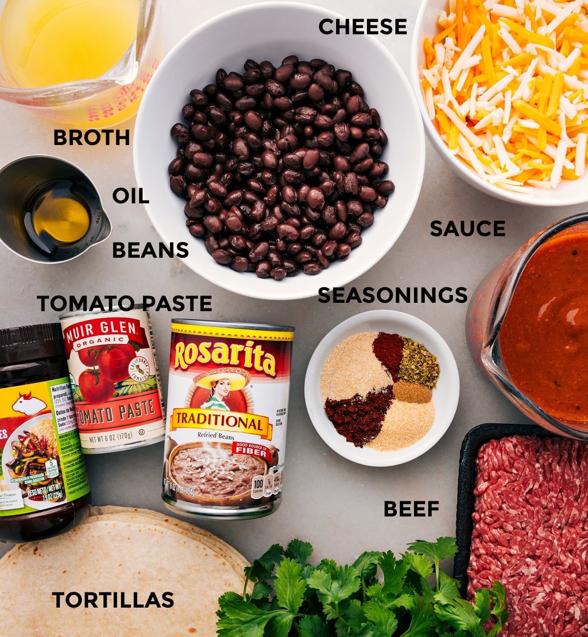 Ingredients In Ground Beef Enchiladas Ingredients prepped for easy assembly—broth, cheese, beans, sauce, seasonings, beef, tomato paste, and tortillas.