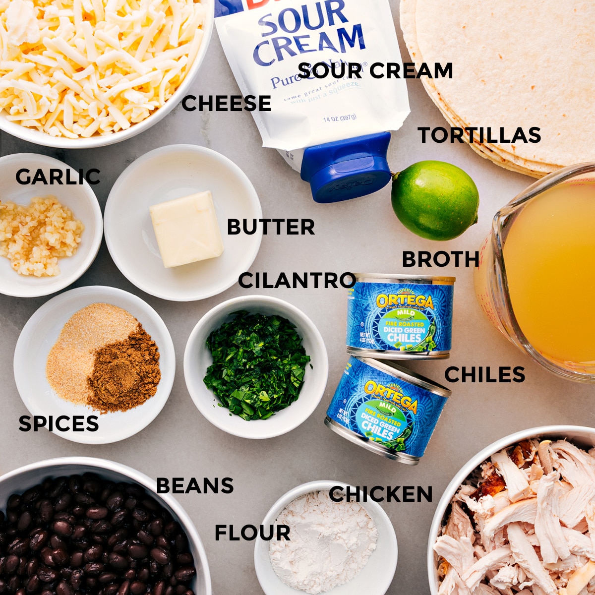 Ingredients In White Chicken Enchiladas All the ingredients prepped and ready for easy assemblyโcheese, tortillas, sour cream, broth, butter, cilantro, green chiles, garlic, spices, beans, chicken, and flour.