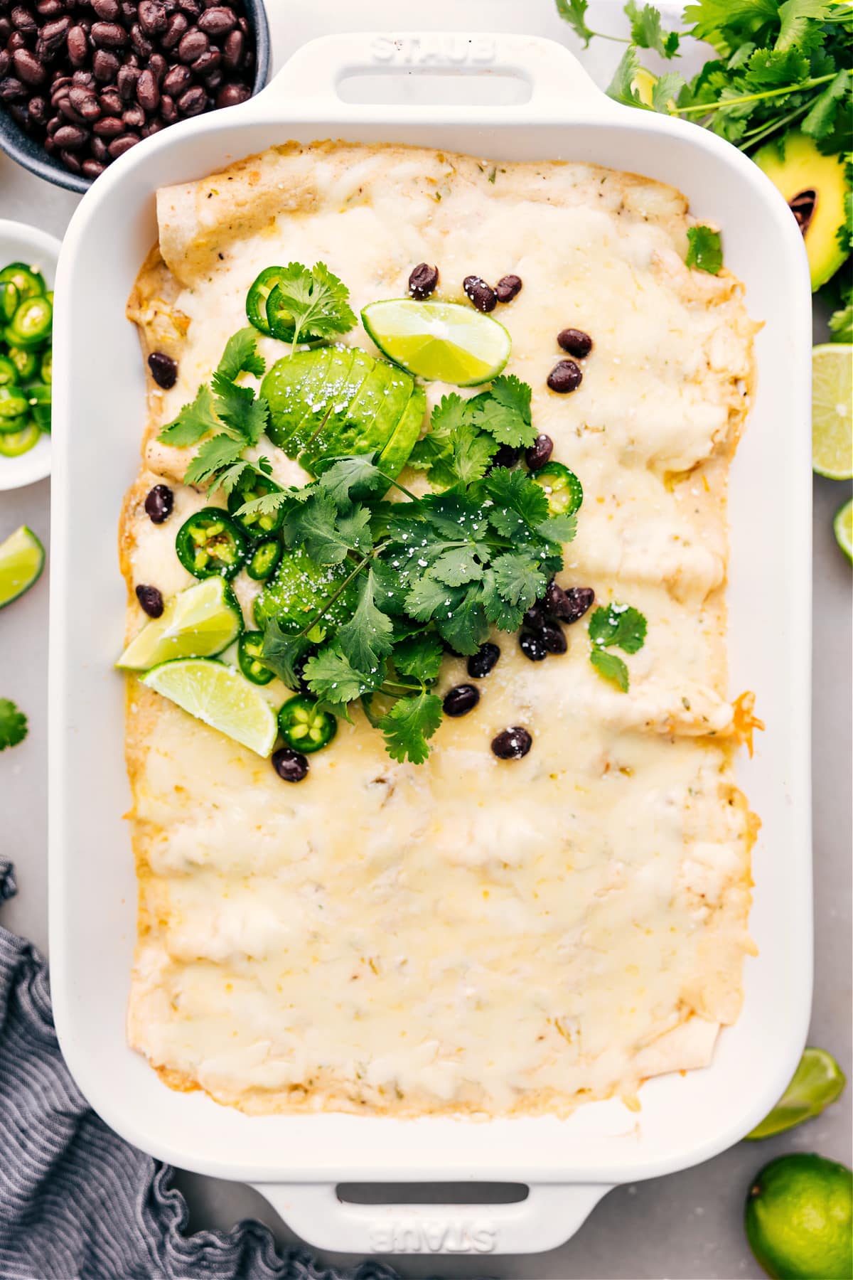 White Chicken Enchiladas in the casserole dish, topped with fresh cilantro, sliced jalapeños, lime wedges, and crumbled cotija.