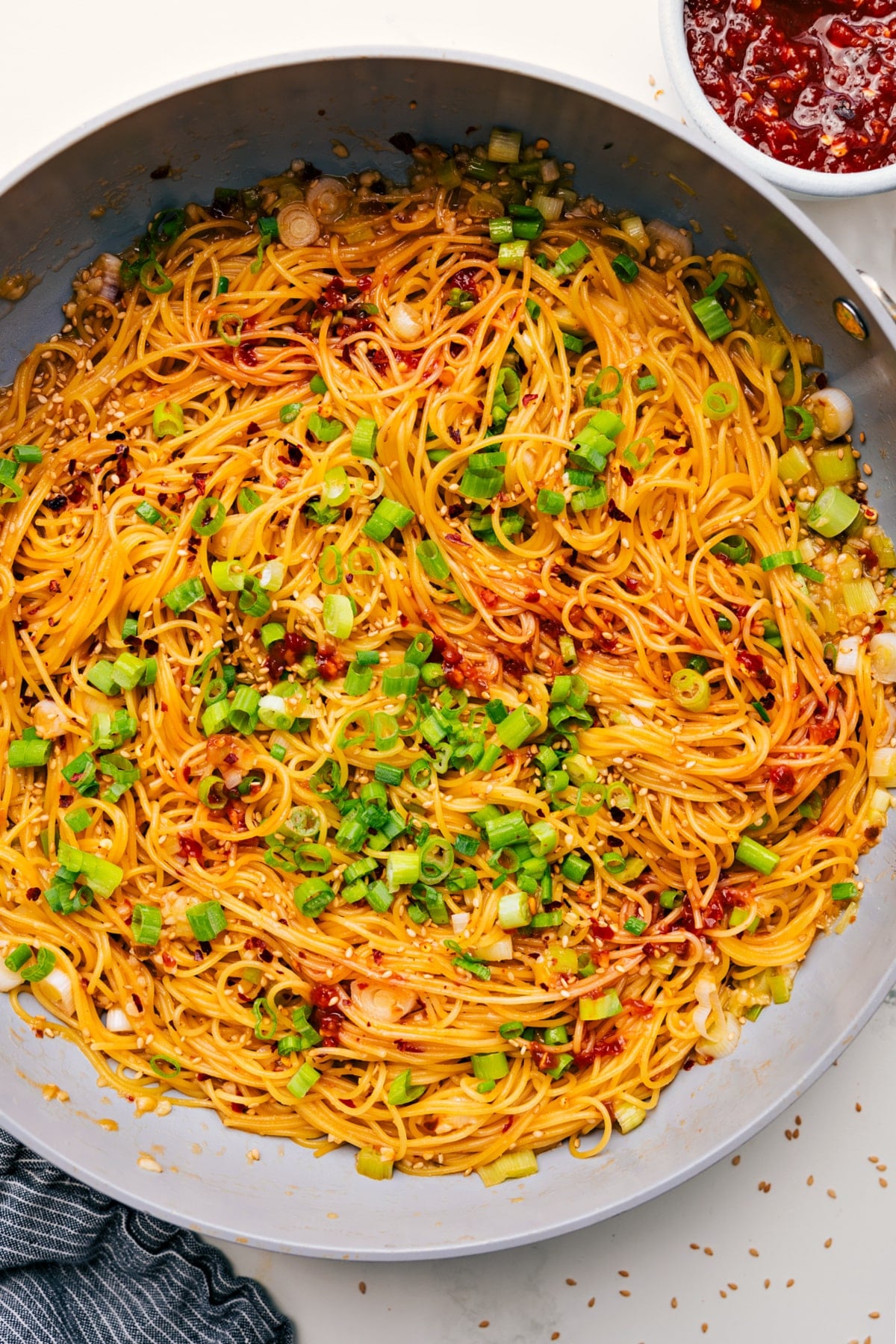 Flavorful And Delicious Chili Garlic Noodles Chili Garlic Noodles in a skillet, garnished with green onions and sesame seeds.