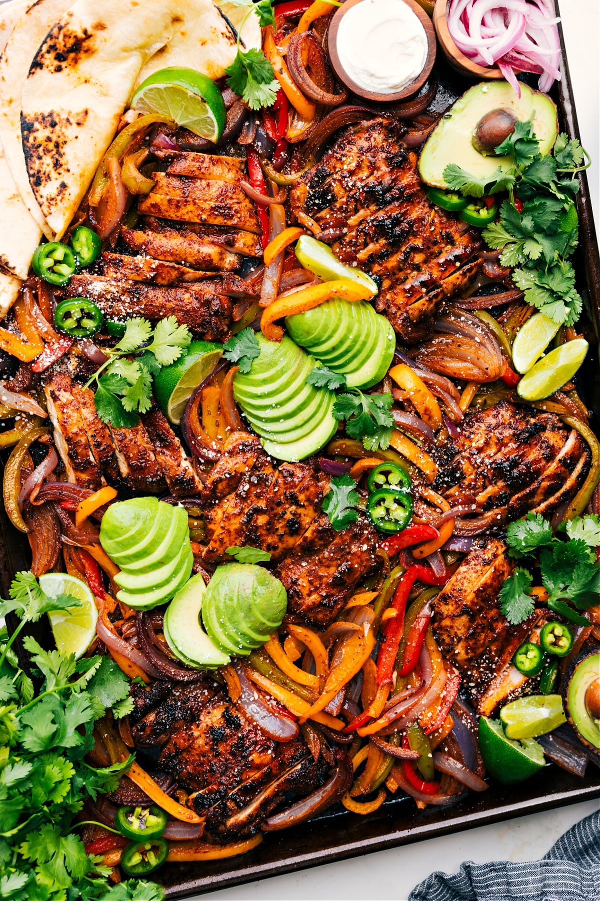 Sheet Pan Chicken Fajitas on the pan topped with fresh avocado, jalapeños, and cilantro.