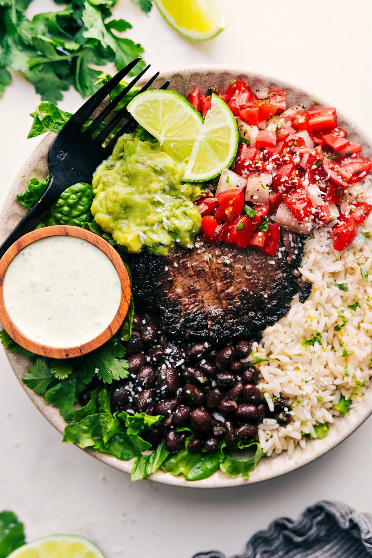 Chipotle steak recipe served in a bowl over rice with black beans, pico de gallo, guacamole, and cilantro lime sauce.