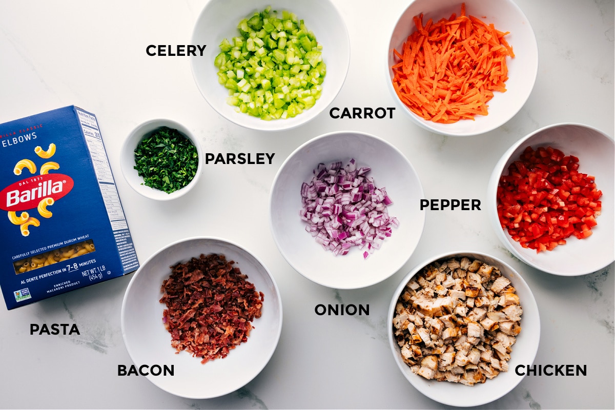 Ingredients In Chicken Macaroni Salad Ingredients in this recipe prepped out for easy assembly including the pasta, parsley, celery, carrot, onion, pepper, chicken, and bacon.