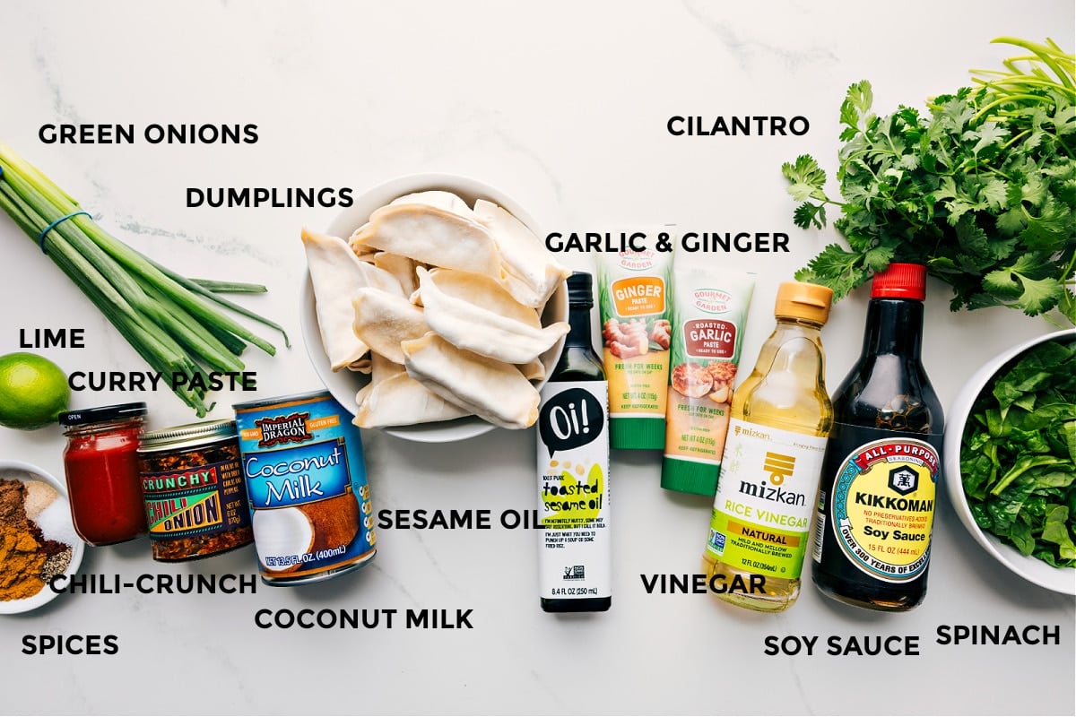Ingredients In One Pan Dumpling Dinner All the ingredients prepped for easy assembly including spices, lime, green onions, dumplings, chili crunch, curry paste, sesame oil, garlic, ginger, cilantro, vinegar, soy sauce, and spinach.