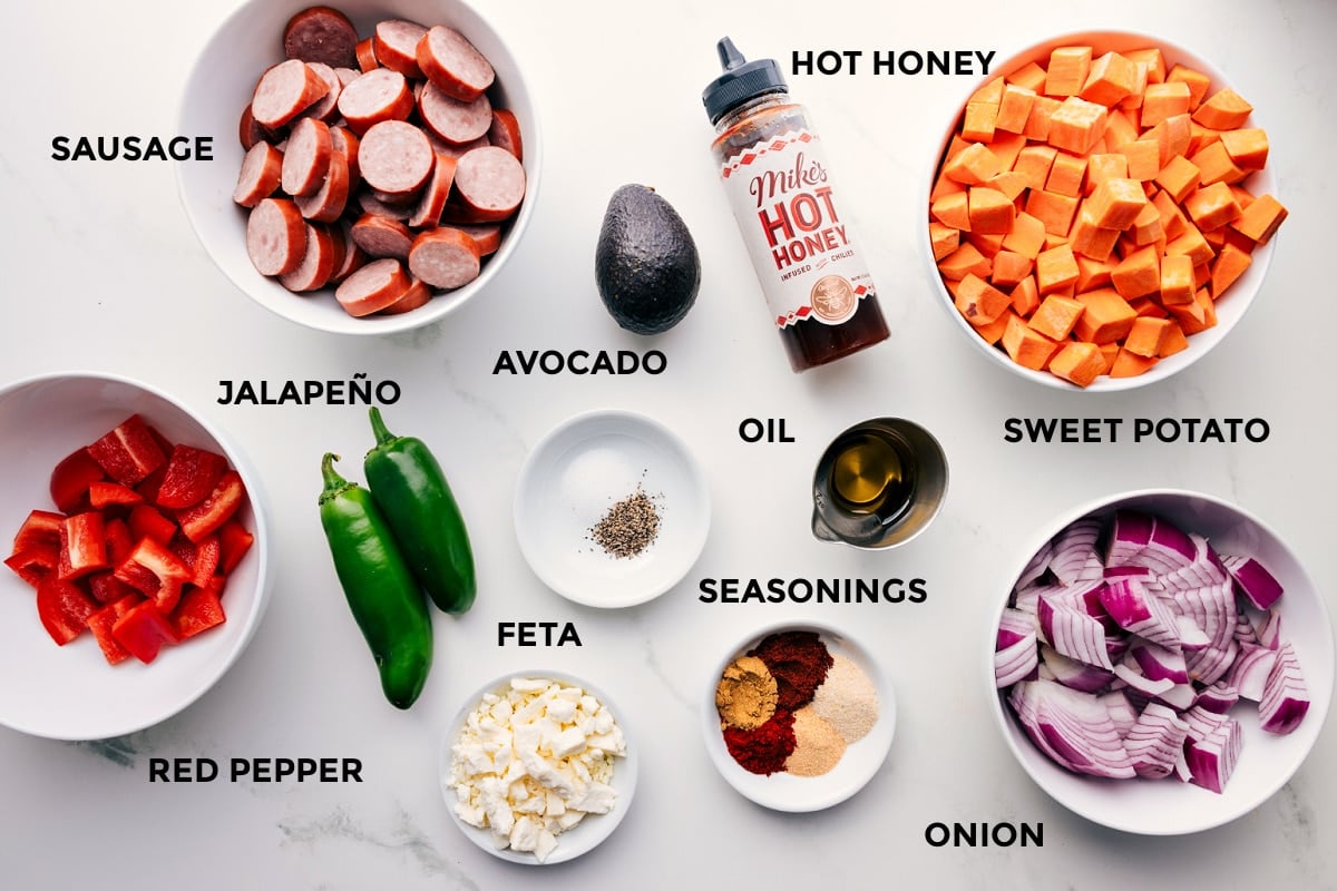 All the ingredients in this recipe prepped out for easy assembly including the red pepper, sausage, jalapeño, feta, avocado, seasonings, oil, hot honey, onion, and sweet potatoes.