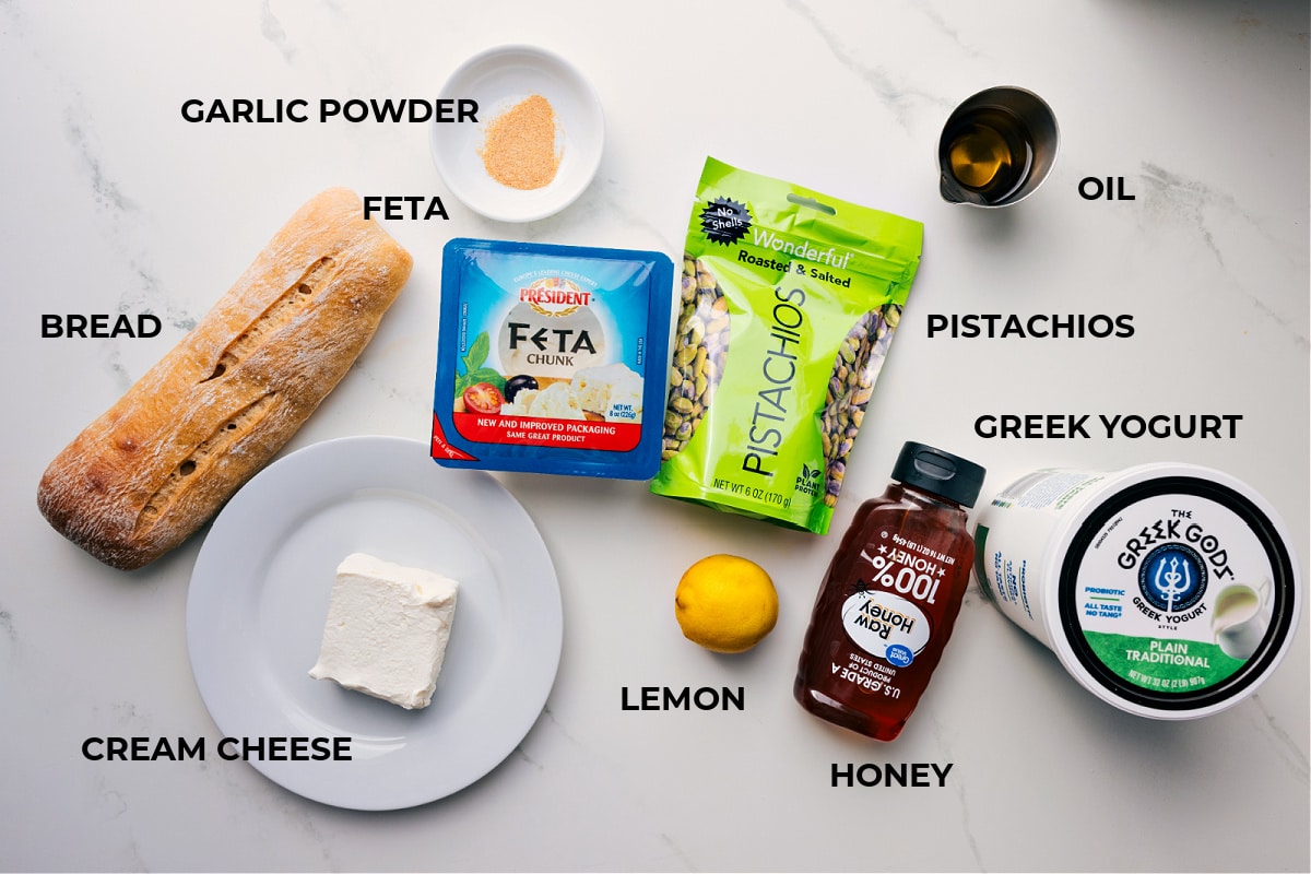 Ingredients In Whipped Feta Recipe All the ingredients in this recipe prepped out for easy assembly including the bread, feta, cheese, pistachios, lemon, honey, yogurt, pistachios, and oil.
