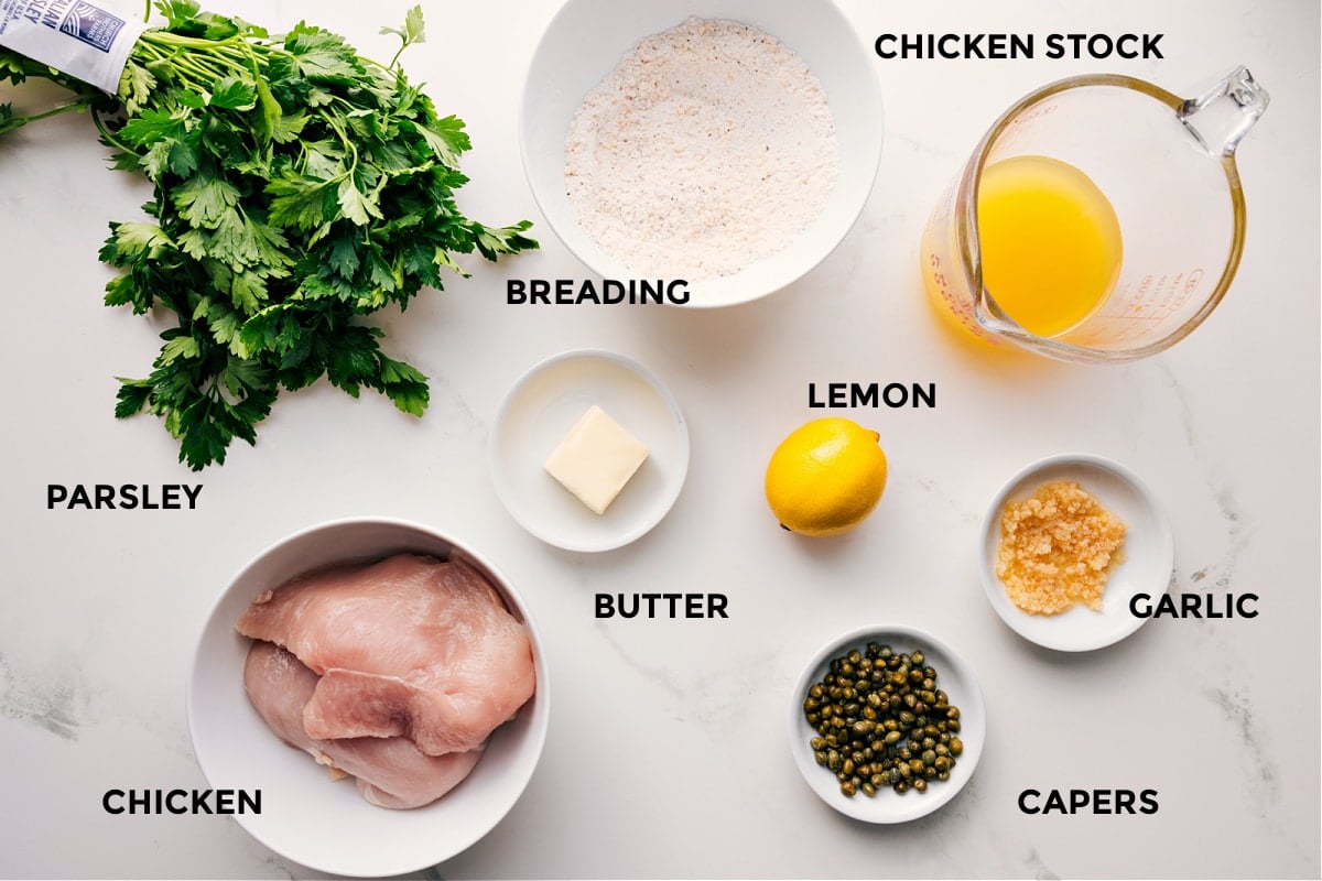Ingredients In Chicken Piccata Ingredients in this recipe prepped for easy assembly including parsley, chicken, breading, butter, lemon, capers, garlic, and stock.