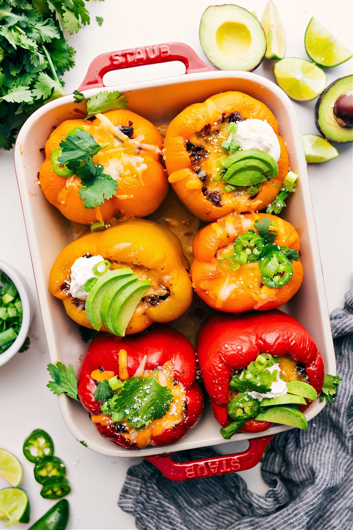 Mexican Stuffed Peppers Is The Perfect Low-Carb Weeknight Dinner Mexican stuffed peppers in a pan topped with fresh cilantro, sliced jalapeños, sour cream, and avocado pieces.