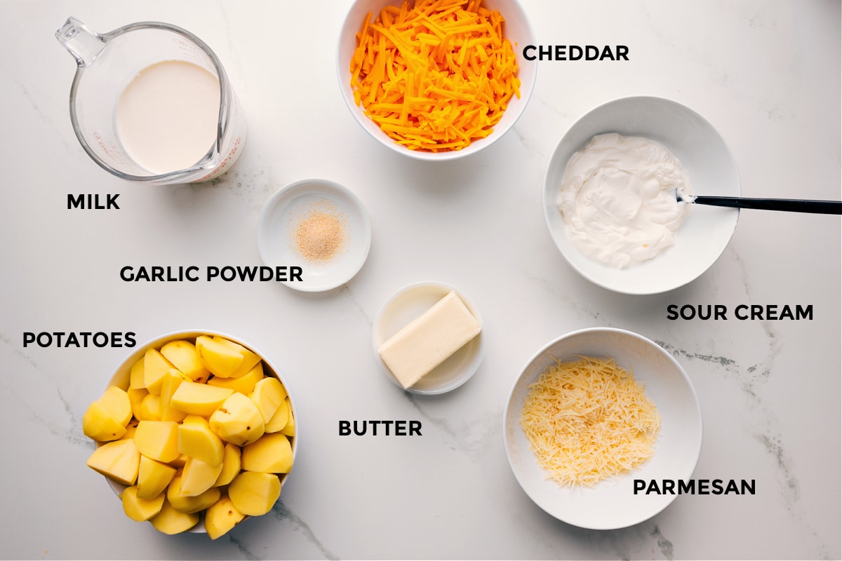 Ingredients In Cheesy Mashed Potatoes All the ingredients in this recipe prepped out for easy assembly including the milk, garlic powder, potatoes, butter, parmesan, sour cream, and cheddar.
