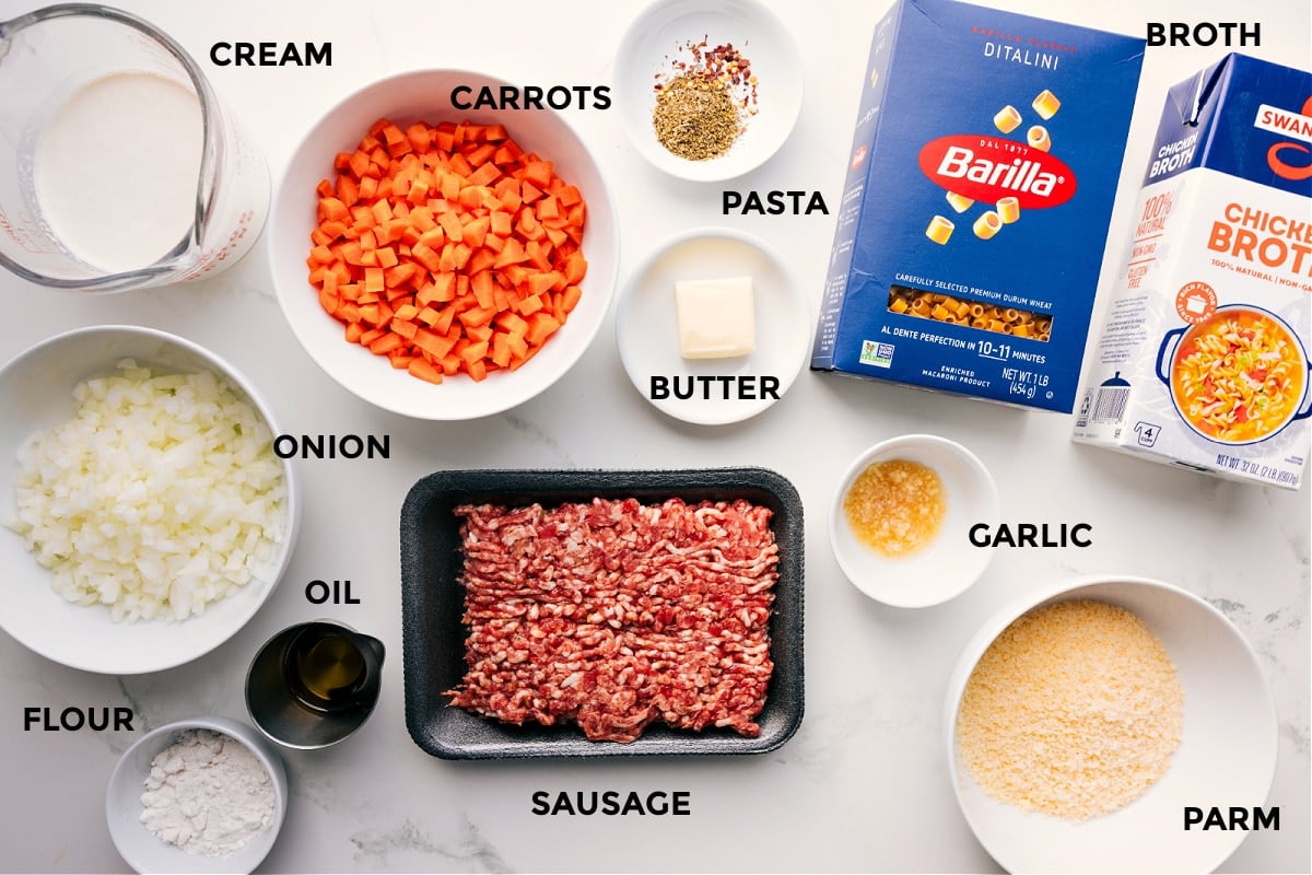 All the ingredients for this recipe prepped and ready, including cream, veggies, flour, oil, sausage, pasta, butter, garlic, Parmesan, and broth.