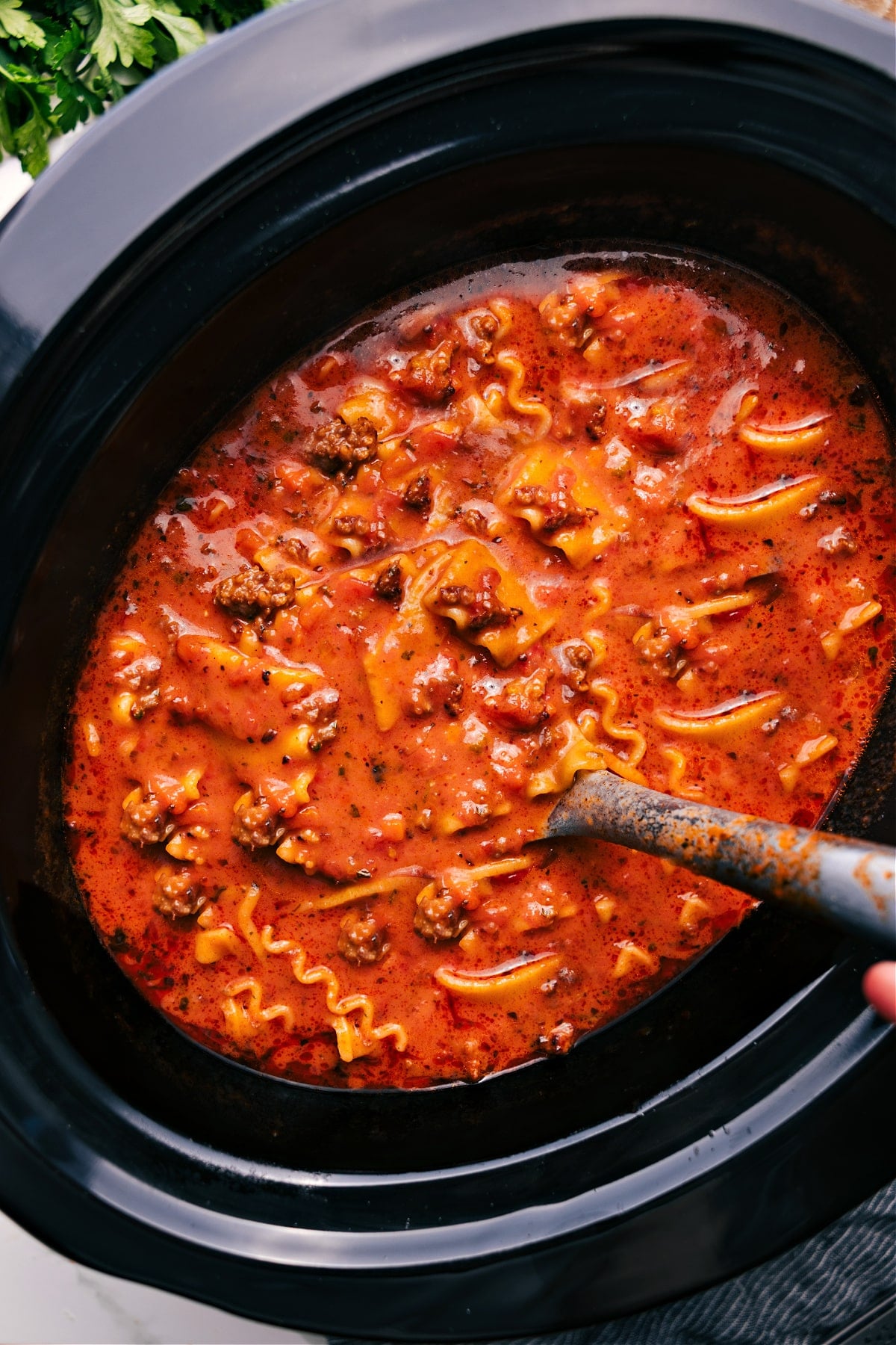 Crockpot Lasagna Soup in a slow cooker with a large scoop being lifted out.