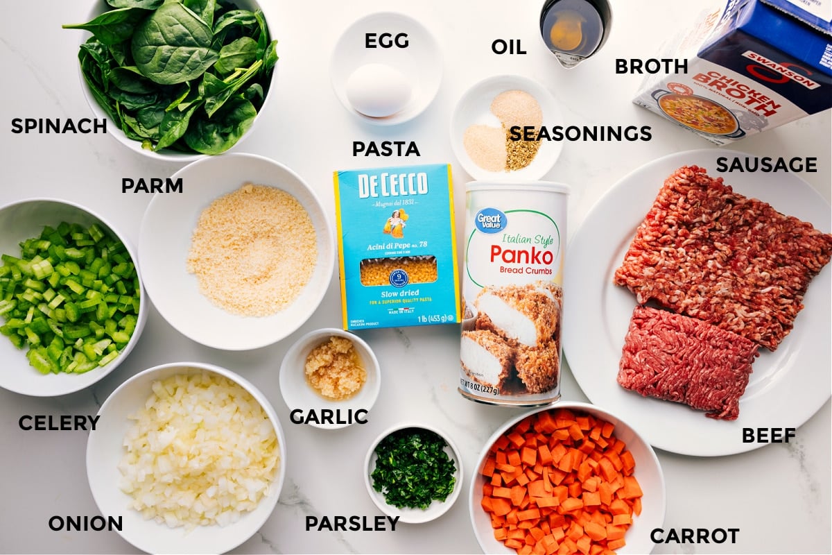 Ingredients In Italian Wedding Soup Recipe Ingredients prepped for easy assembly including spinach, celery, onion, Parmesan, garlic, parsley, carrots, panko, beef, sausage, broth, seasonings, oil, egg, and pasta.