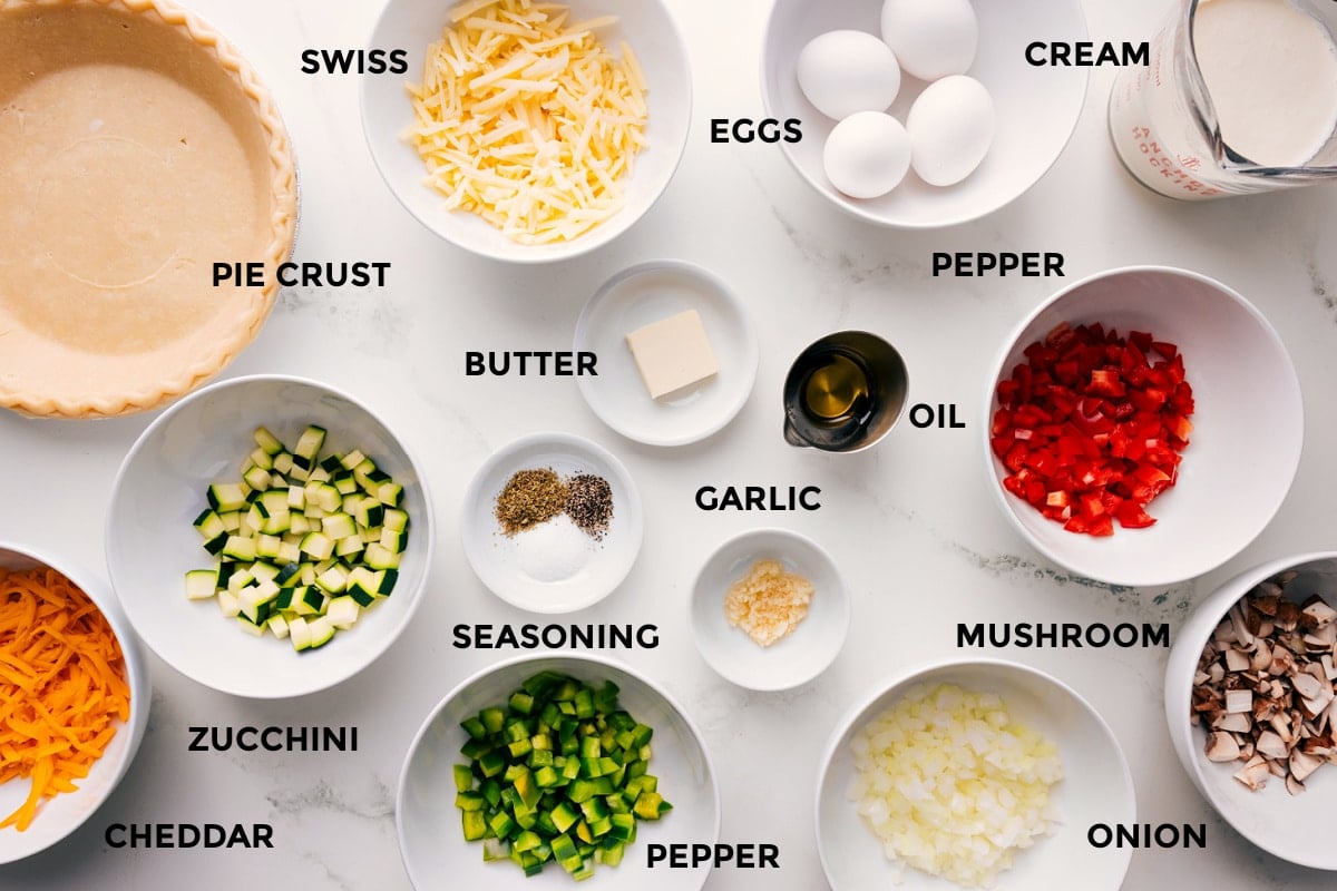 Ingredients In Veggie Quiche Recipe All the ingredients prepped and ready, including the pie crusts, cheese, zucchini, butter, seasonings, garlic, oil, onion, mushrooms, peppers, cream, and eggs.