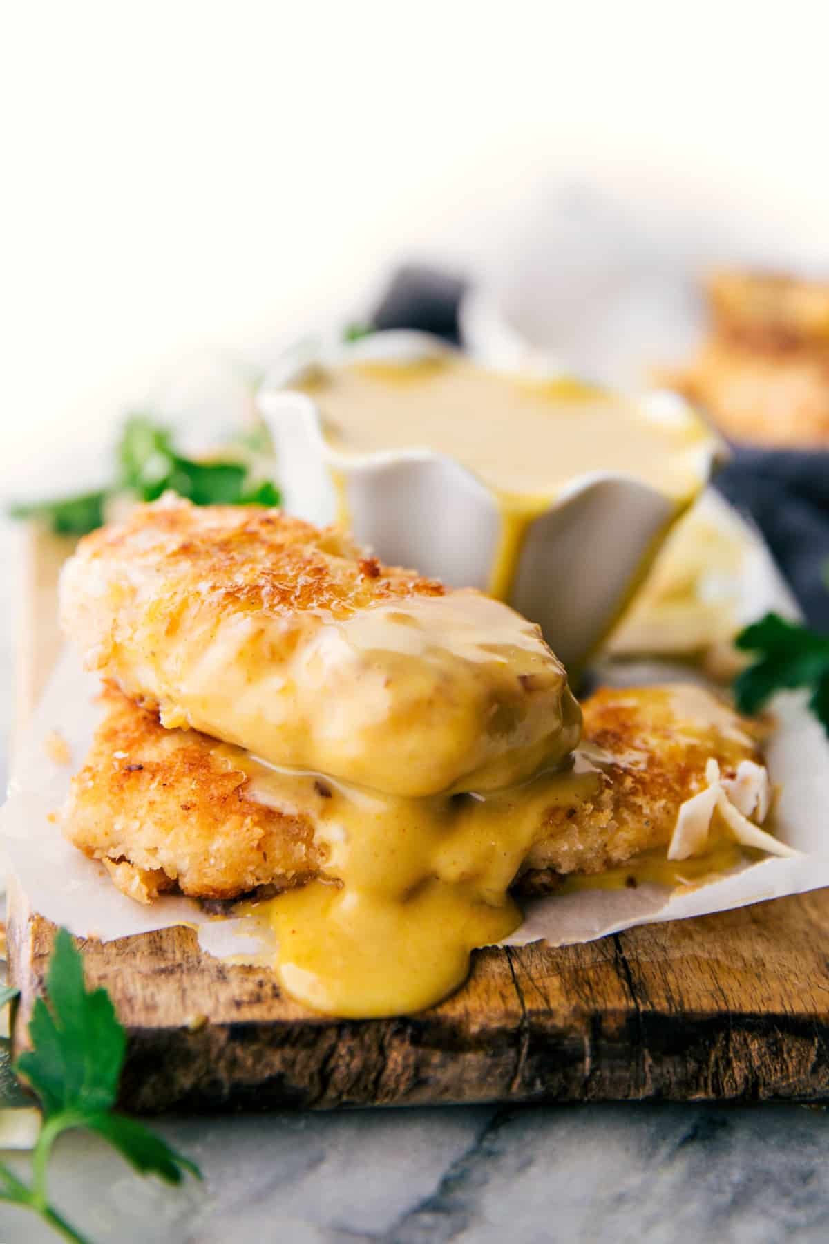 Coconut chicken tenders stacked on top of each other with the best honey mustard sauce on top.