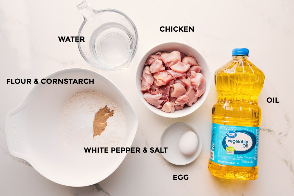 Korean Chicken Recipe Ingredients Needed Korean chicken recipe ingredients prepped out for easy assembly including the flour, cornstarch, water, chicken, white pepper, salt, egg, and oil.