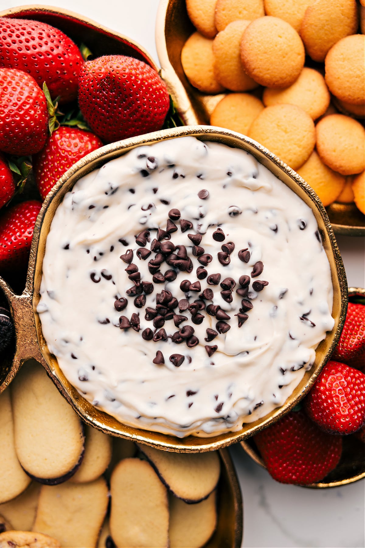 Chocolate Chip Dip in a bowl topped with chocolate chips, surrounded by strawberries and cookies for dipping.