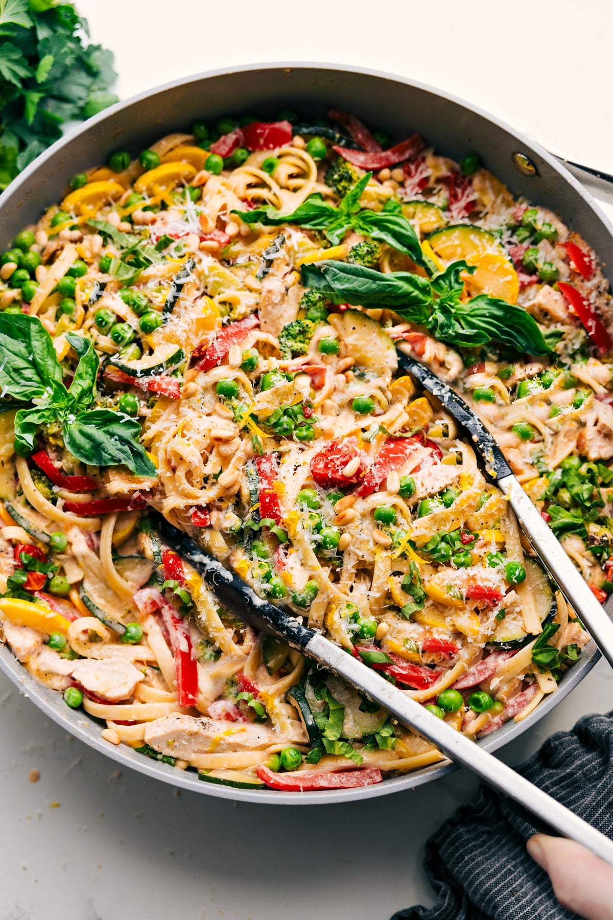 Creamy, Flavorful, And Delicious Chicken Primavera Chicken Primavera in a pot with tongs lifting a portion to serve.