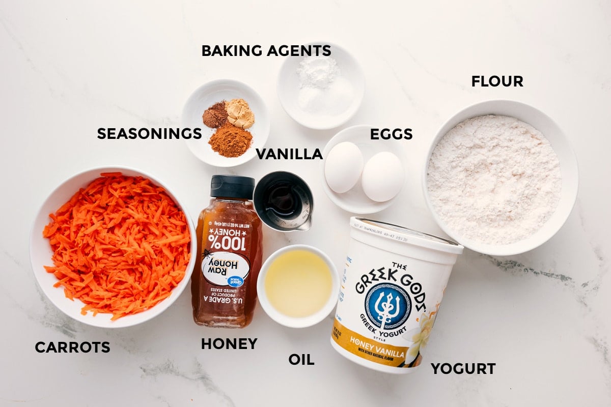 Ingredients In These Healthy Carrot Muffins All the ingredients in this recipe prepped out for easy assembly including the carrots, seasonings, honey, oil, yogurt, flour, eggs, vanilla, and the baking agents.