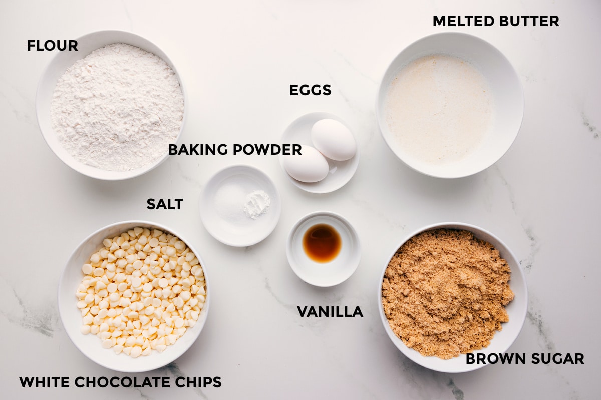 Ingredients In This Sugar Cookie Bars Recipe All. the ingredients in this recipe prepped out for easy assembly including the flour, white chocolate chips, salt, baking powder, eggs, vanilla, melted butter, and brown sugar.