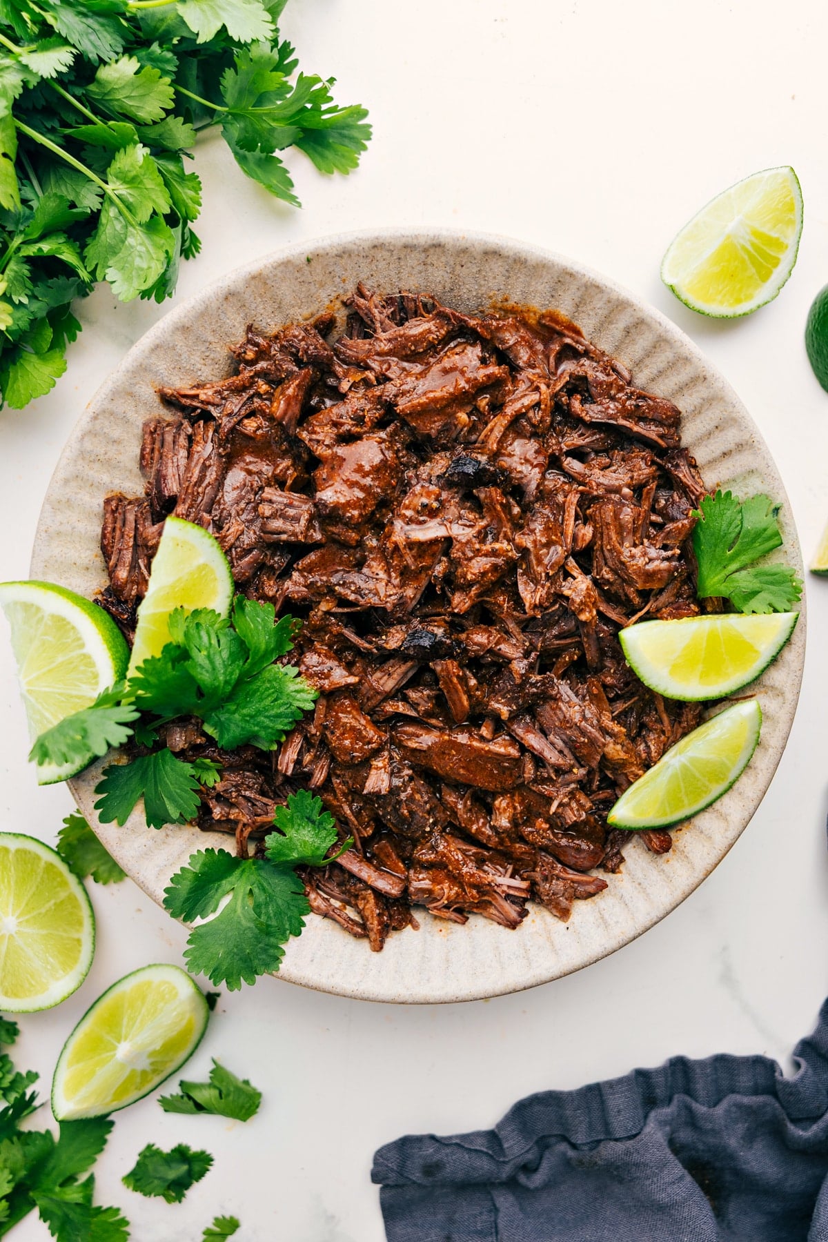 Barbacoa Beef Recipe in a bowl fresh from the slow cooker with lime wedges and cilantro on the side.