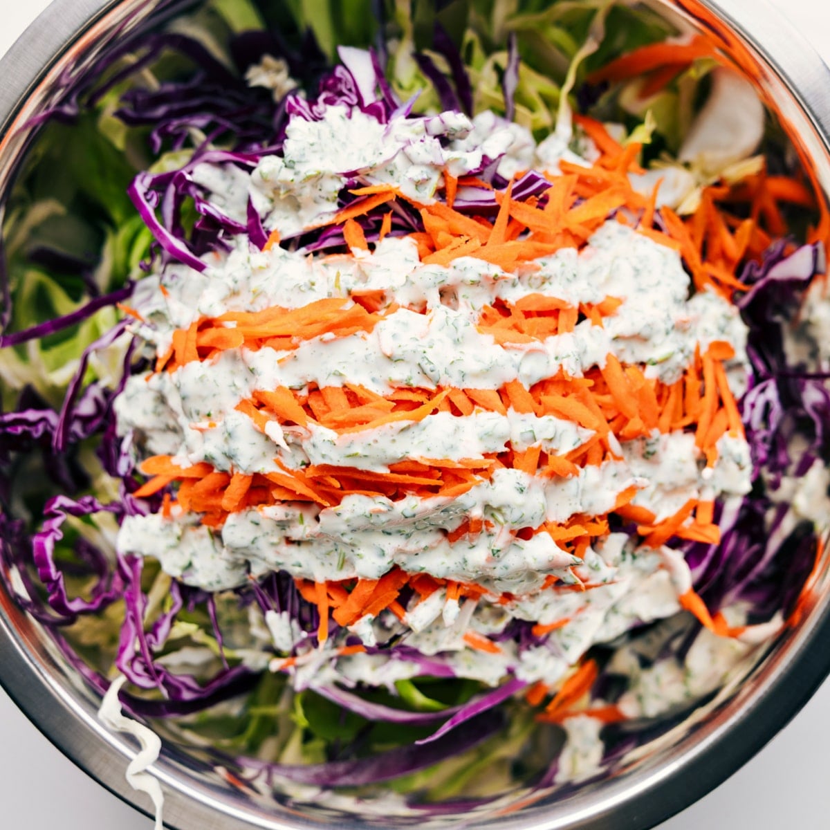 Mexican Slaw Recipe That Everyone Loves All the ingredients added to a large bowl with the dressing drizzled on top.