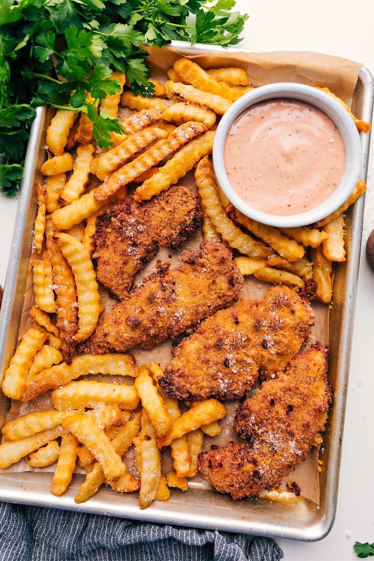 Parmesan Chicken Tenders on a tray with fries and dipping sauce.