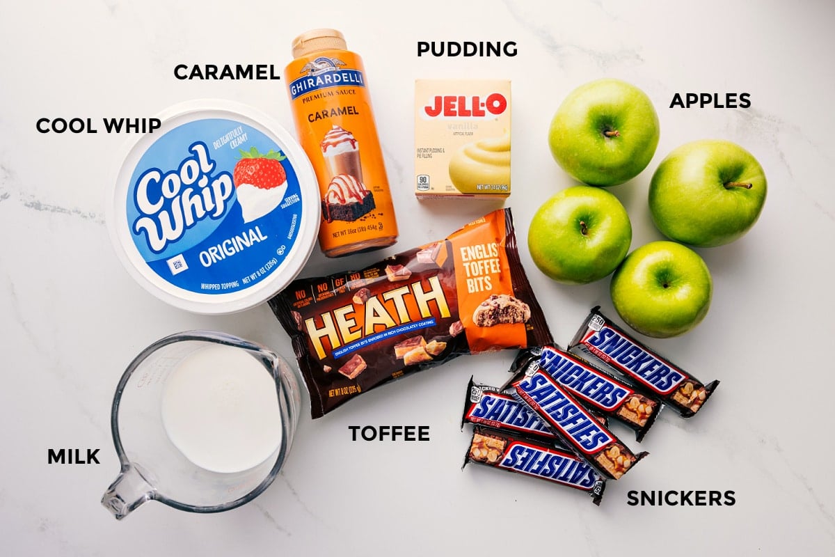 Ingredients In This Snickers Salad Recipe All the ingredients in this recipe prepped out for easy assembly including the milk, cool whip, caramel, toffee, snickers, apples, and jello.