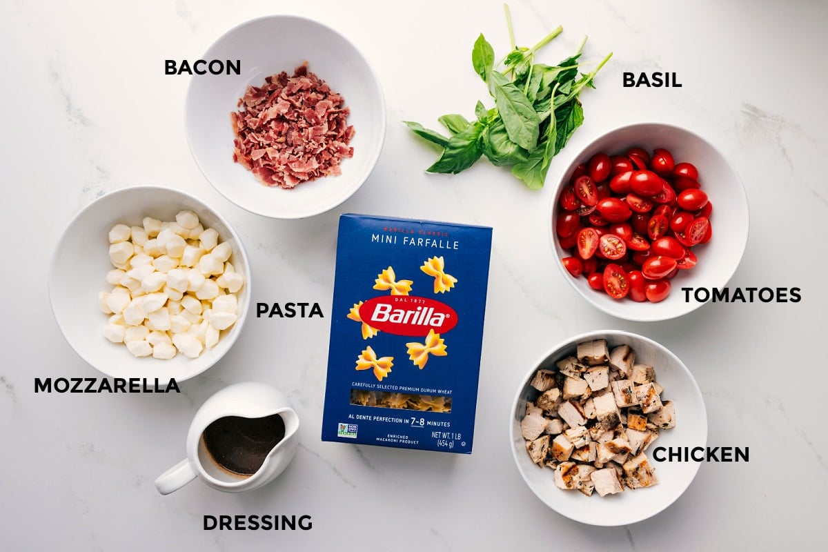 Ingredients In Caprese Pasta Salad All the ingredients in this recipe prepped out for easy assembly including the bacon, mozzarella, dressing, pasta, chicken, tomatoes, and basil.